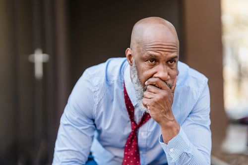 Free Unhappy bearded African American male worker in classy wear with hand on mouth looking away with concern while sitting on street Stock Photo