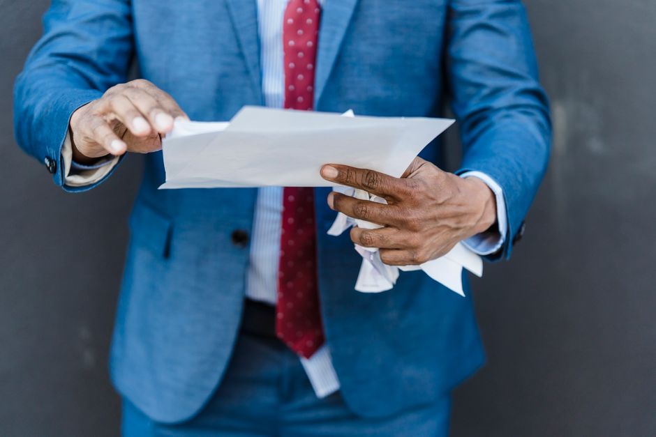 Crop anonymous businessman in classy suit with documents and crumpled paper in hands standing on gray background in city after hard workday