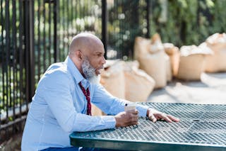 Side view of concerned African American male entrepreneur in formal clothes with can of alcohol beverage sitting at table on street
