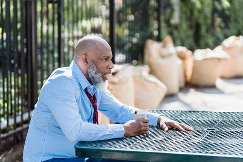 Free Side view of concerned African American male entrepreneur in formal clothes with can of alcohol beverage sitting at table on street Stock Photo