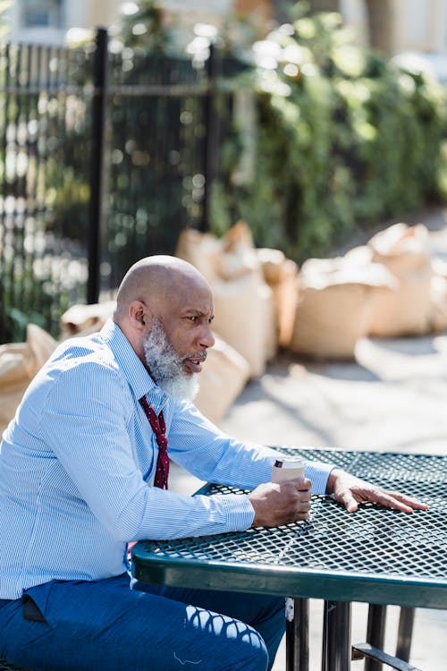 Side view of sad bearded African American male entrepreneur in alcohol drink sitting at table on street in city