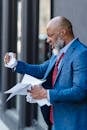 Side view of furious African American male entrepreneur in formal wear with documents in hands standing on street near building