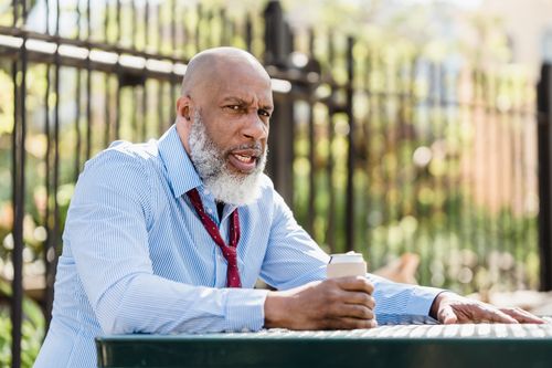 Free Concentrated mature African American male with blue shirt and untied tie sitting at table with tin can of beverage at terrace of cafe Stock Photo
