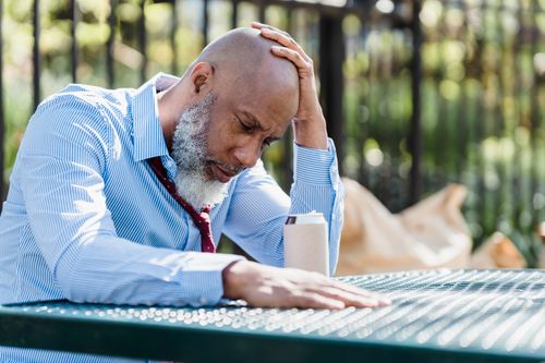 Free Concentrated African American man in trendy shirt grabbing head with hand sitting with closed eyes at table with beverage in tin can in terrace of cafe in sunlight Stock Photo