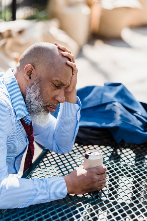 Free From above of thoughtful African American male in trendy classy outfit sitting with beverage in tin can and leaning head on hand in terrace cafe Stock Photo