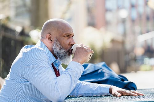 Free Senior man with beard relaxes while sipping coffee outdoors in a park setting. Stock Photo