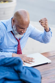 Elderly businessman triumphantly celebrates success with clenched fist at an outdoor café.