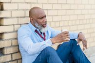 Troubled black man sitting on ground at brick wall