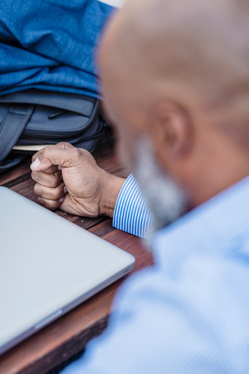 Concentrated bearded African American male clenching hand into fist sitting at table with closed laptop