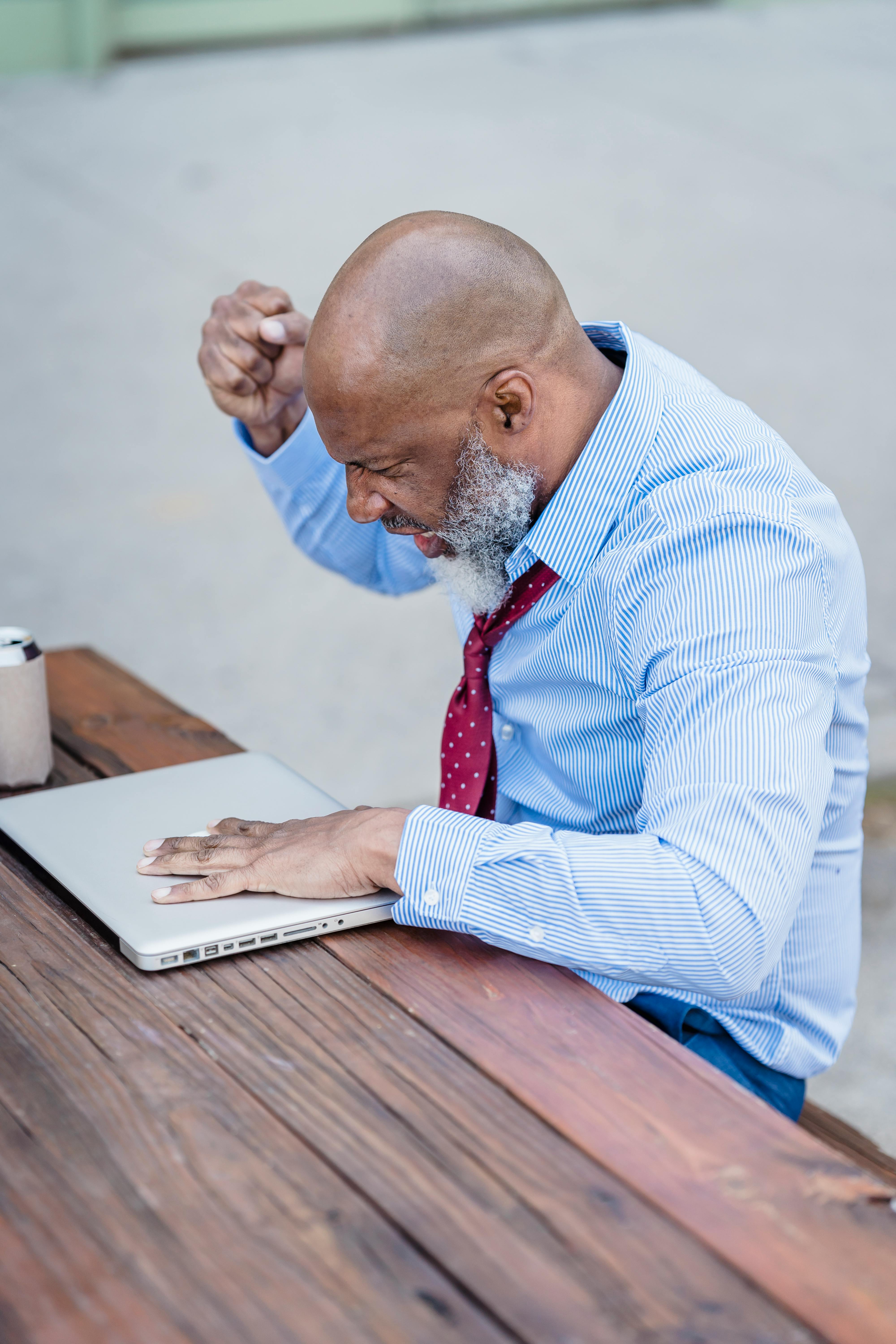 aged bearded black man freelancer sitting at table with laptop