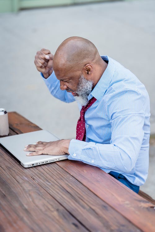 Free Concentrated bald senior bearded male entrepreneur sitting at table with closed laptop and thinking over project Stock Photo