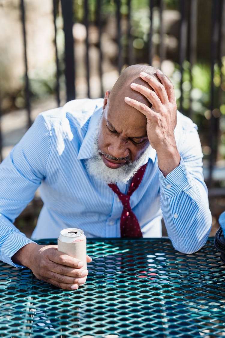 Troubled Senior Black Man Sitting At Table With Tin Can