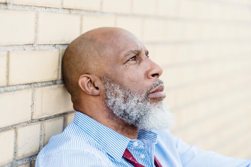 Free Side view of hairless bearded African American man in t shirt thinking near brick wall and looking away Stock Photo