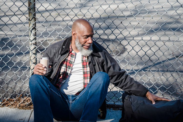 Senior Man With Beer Can And Bag Near Wire Fence