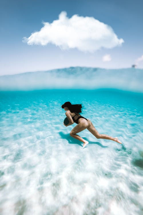 Free Full body side view of female tourist swimming in transparent blue sea with sandy bottom during summer vacation Stock Photo