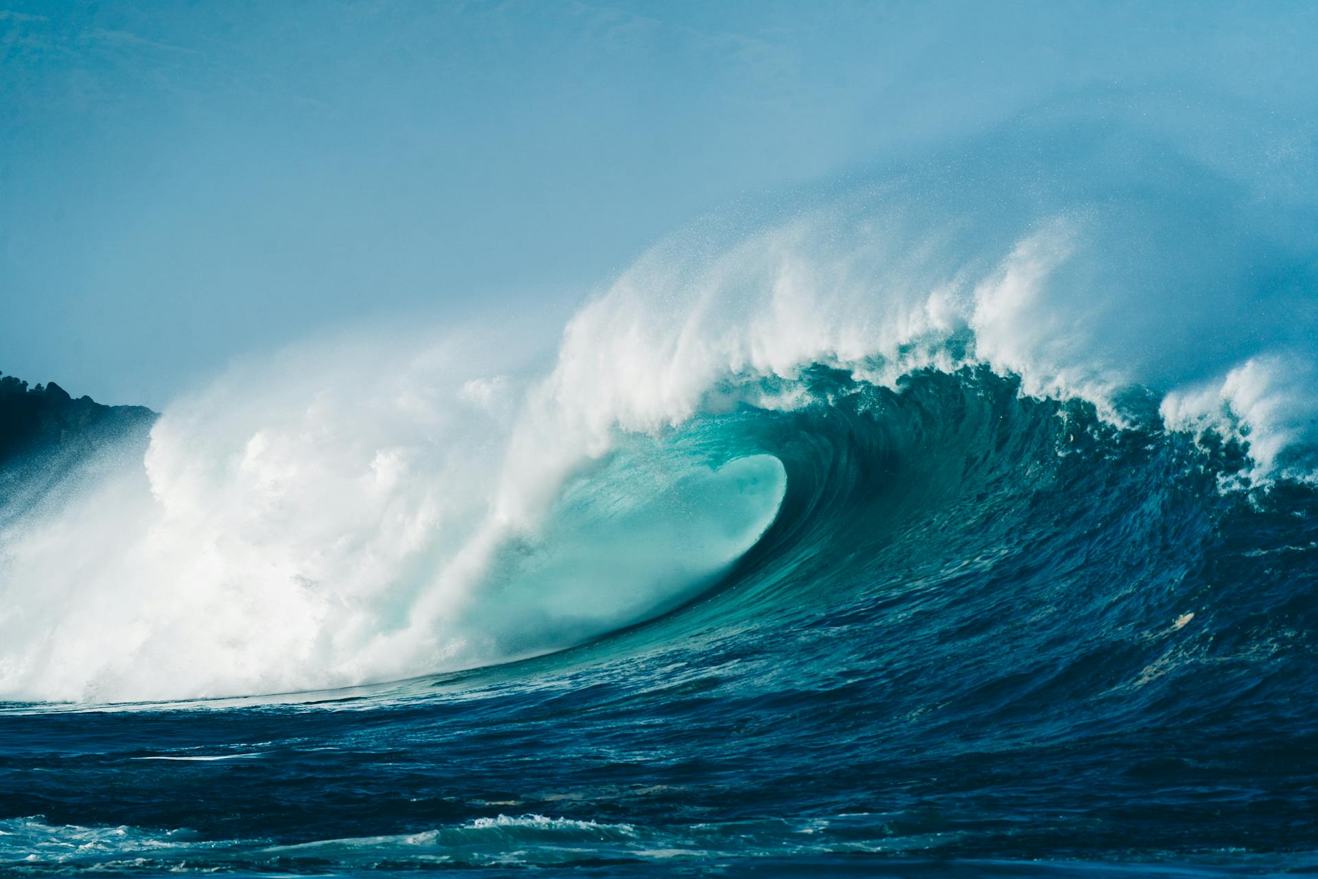 Powerful wave rolling and splashing on turquoise sea surface beneath clear blue sky on sunny day