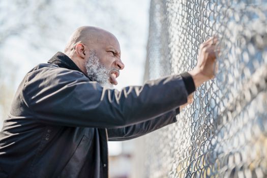 A frustrated man passionately grips a chain-link fence, expressing stress and determination.