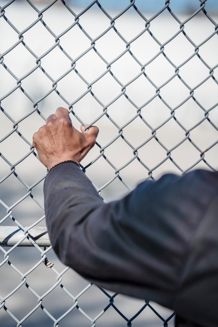 Man Clenching Hand On Fence Net