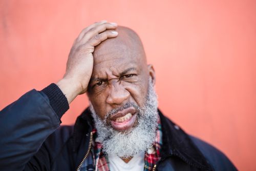 Free Close-up portrait of a bald, bearded man with a hand on his head, expressing emotion against a peach background. Stock Photo