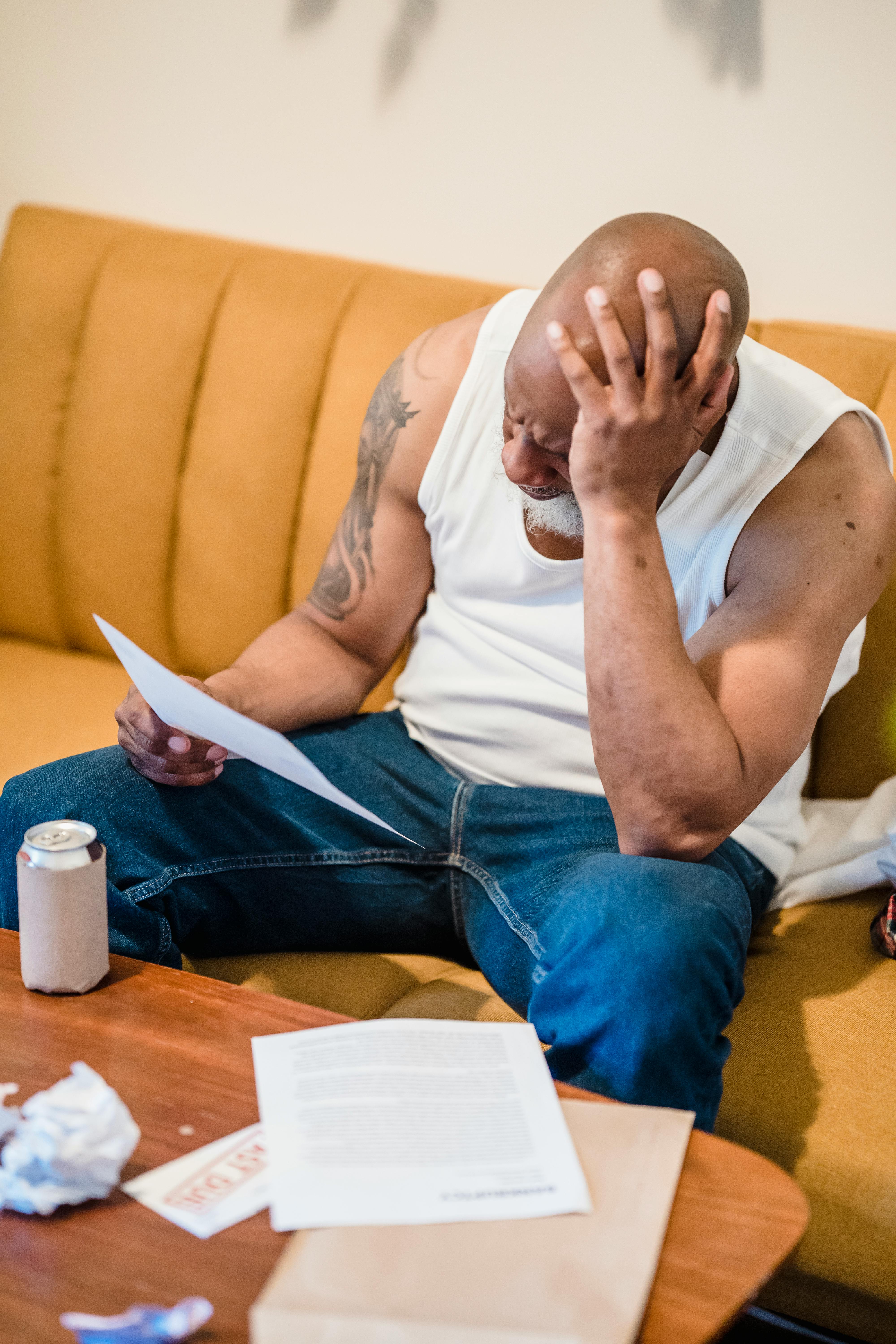 An adult man looking stressed as he reviews bills and documents in his living room.