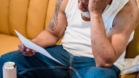 An adult man looking stressed as he reviews bills and documents in his living room.