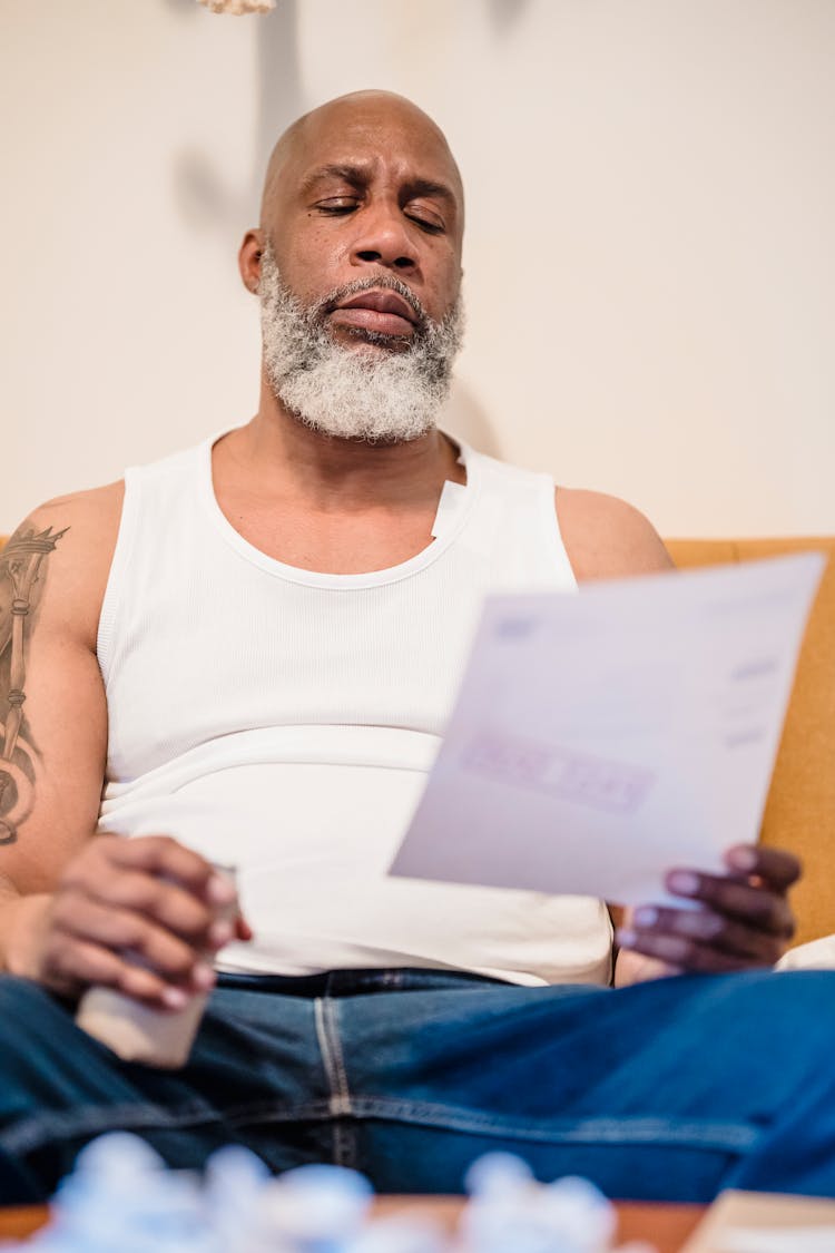 Old Man Sitting On Sofa Reading Document