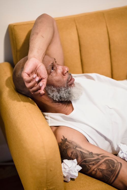 Free Portrait of a tattooed man relaxing on a sofa, lost in thought. Perfect for themes of relaxation and contemplation. Stock Photo