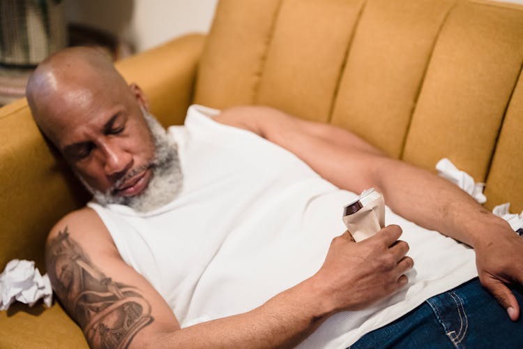 Bearded Man With A Tattoo Sleeping On Sofa With Trash