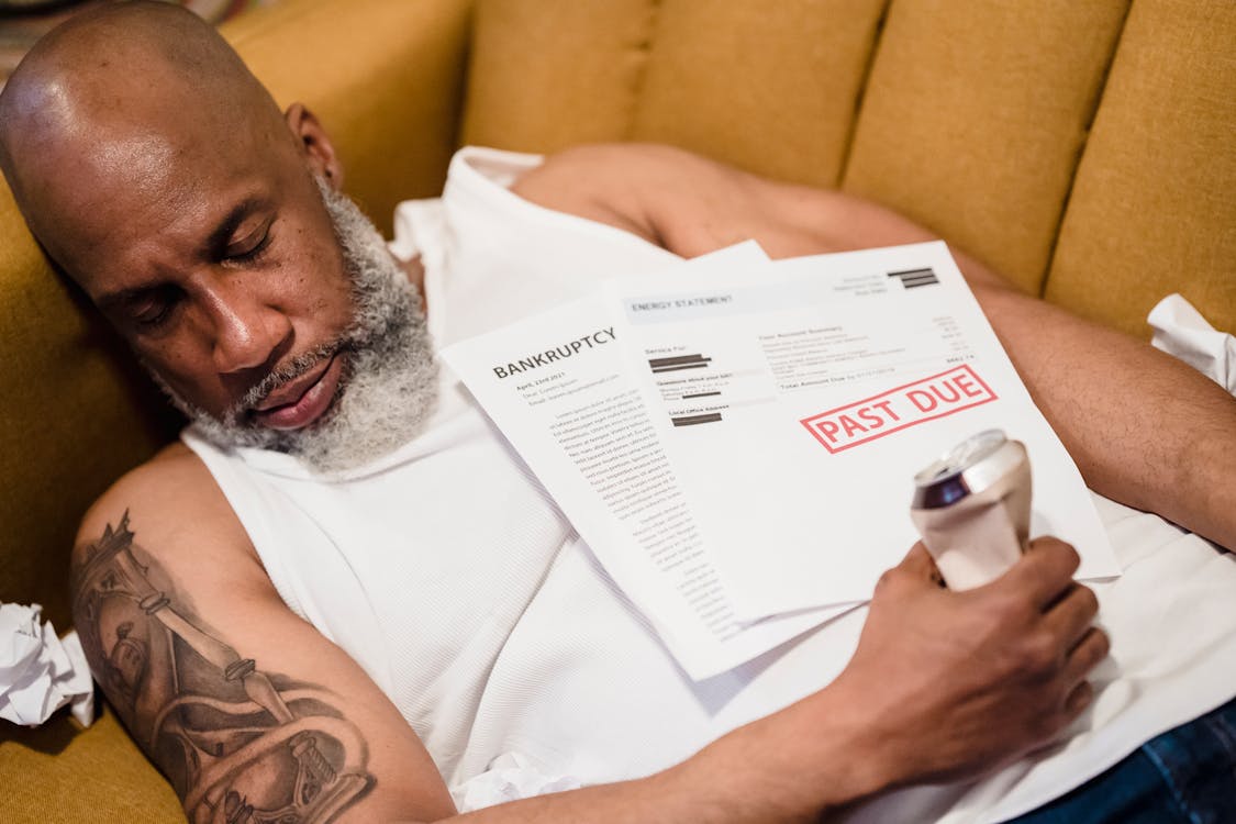 Free Bearded Man with a Tattoo Sleeping with an Alcohol Can and Unpaid Bills Stock Photo