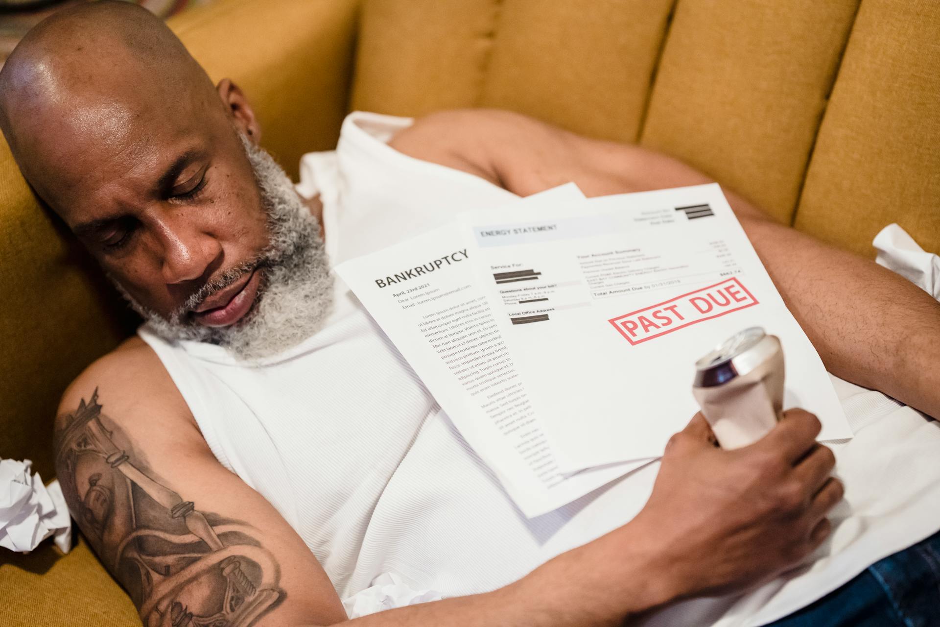 Bearded Man with a Tattoo Sleeping with an Alcohol Can and Unpaid Bills