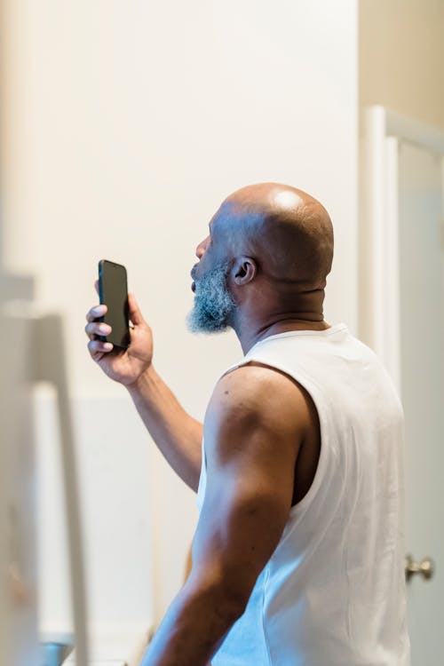 Man in White Tank Top Holding Black Smartphone