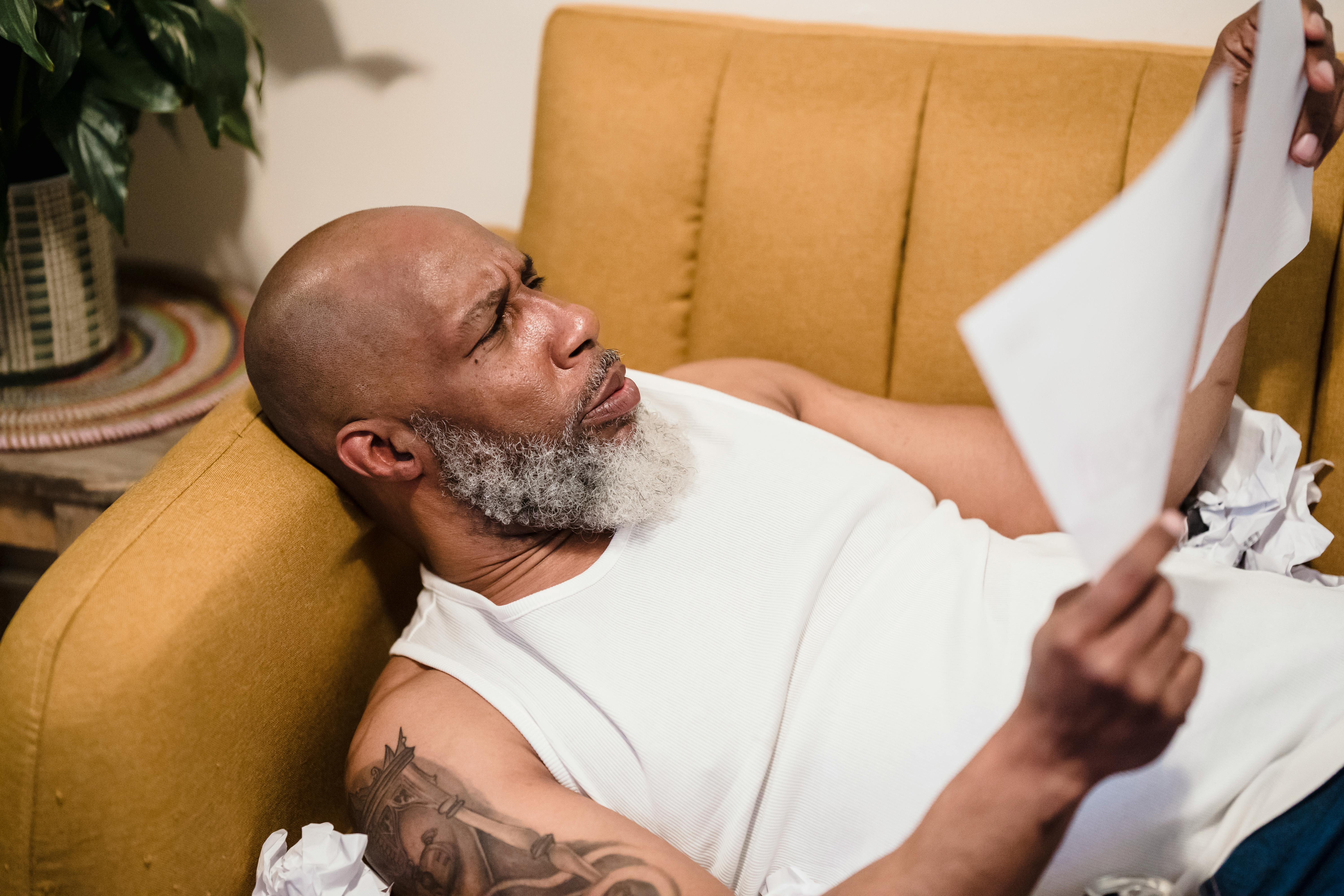 man lying down on sofa and looking with disbelief at documents