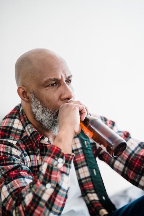 Free A thoughtful man holding a beer bottle, sitting indoors, wearing a plaid shirt. Stock Photo