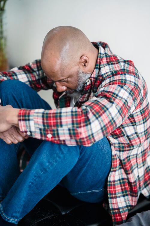 Free A bald man in a checkered shirt sits indoors, looking contemplative and sad. Stock Photo