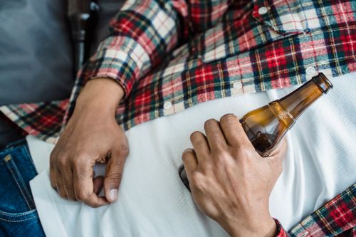 Free Close-up of a relaxed man holding a beer bottle while lying down indoors on a casual day. Stock Photo