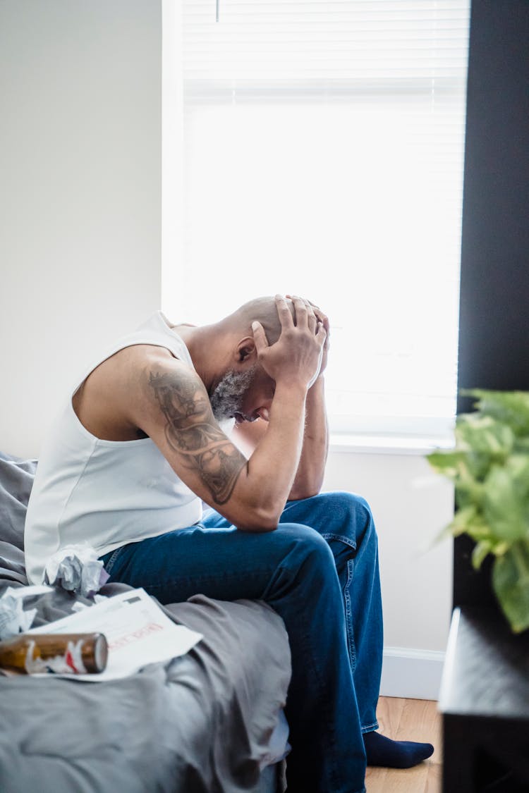 Man Sitting On Bed Holding Head In Hands