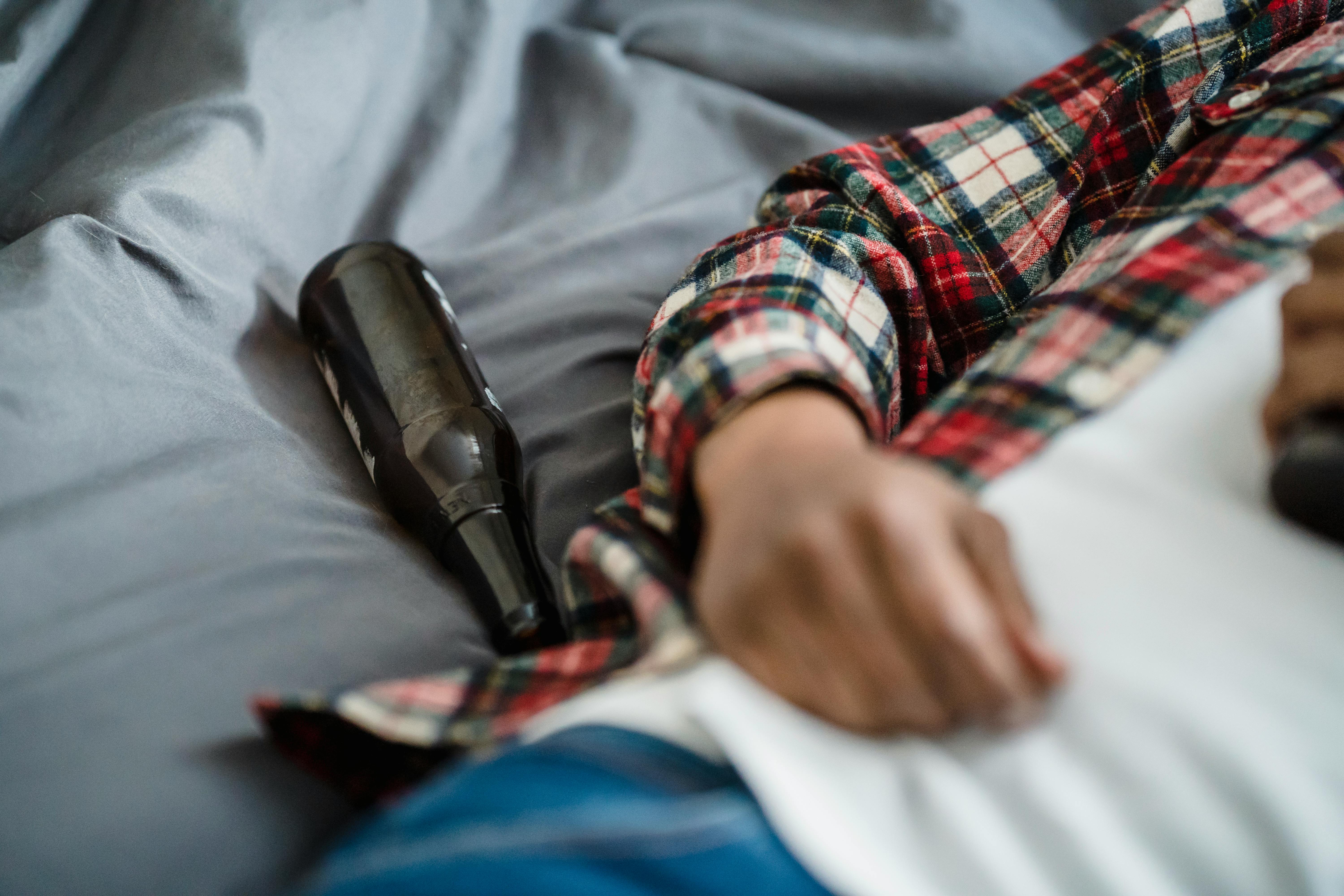 A person lying down with a beer bottle on the bed, wearing casual clothes.