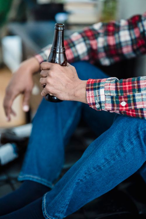 Free Person in casual attire holding a beer bottle indoors, emphasizing relaxation. Stock Photo