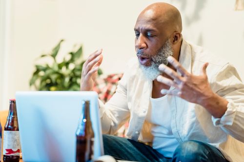 Free Adult man using laptop for video call, gesturing, with beers nearby indoors. Stock Photo
