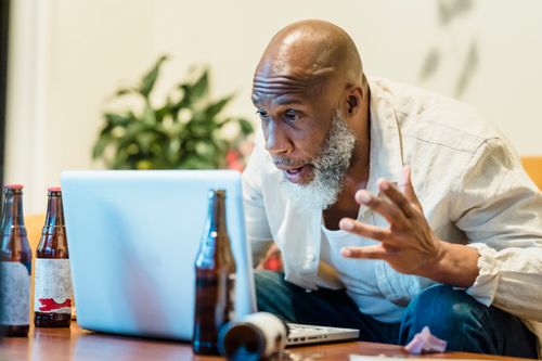 Free Bald man with a beard intensely focused on his laptop, surrounded by beer bottles indoors. Stock Photo