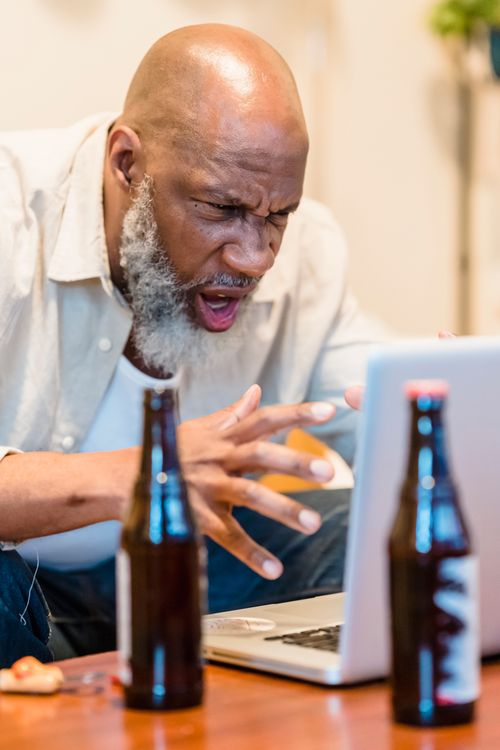 Free A bearded man showing frustration during a video call with beer bottles on a table. Stock Photo