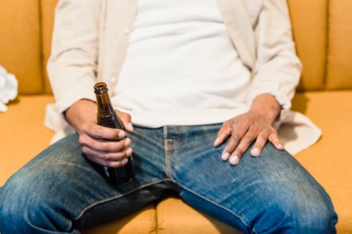 Free Person sitting on a couch holding a beer bottle, dressed in casual attire. Stock Photo