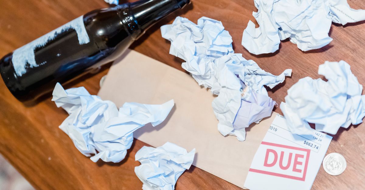 A chaotic scene with overdue bill, beer bottles, and crumpled papers on a wooden table.