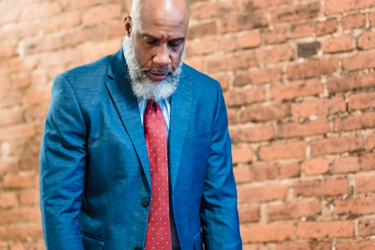 Unhappy Old Man In Suit Near Brick Wall