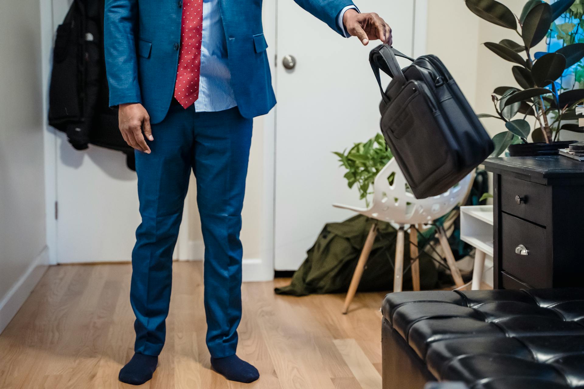 A businessman in a blue suit returns home, holding a briefcase in a cozy living room.