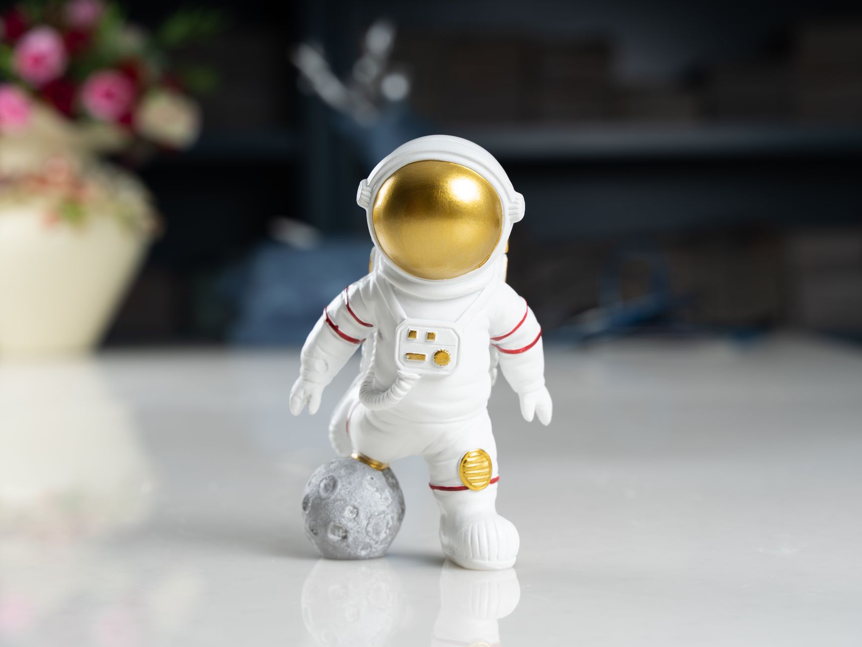 Close-up of a cute miniature astronaut figurine standing on a reflective surface indoors.