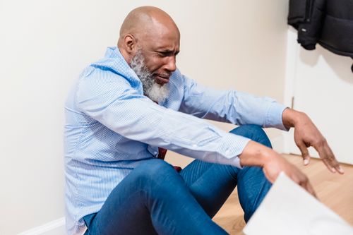 Free An emotional adult man sitting on a wooden floor, expressing vulnerability. Stock Photo