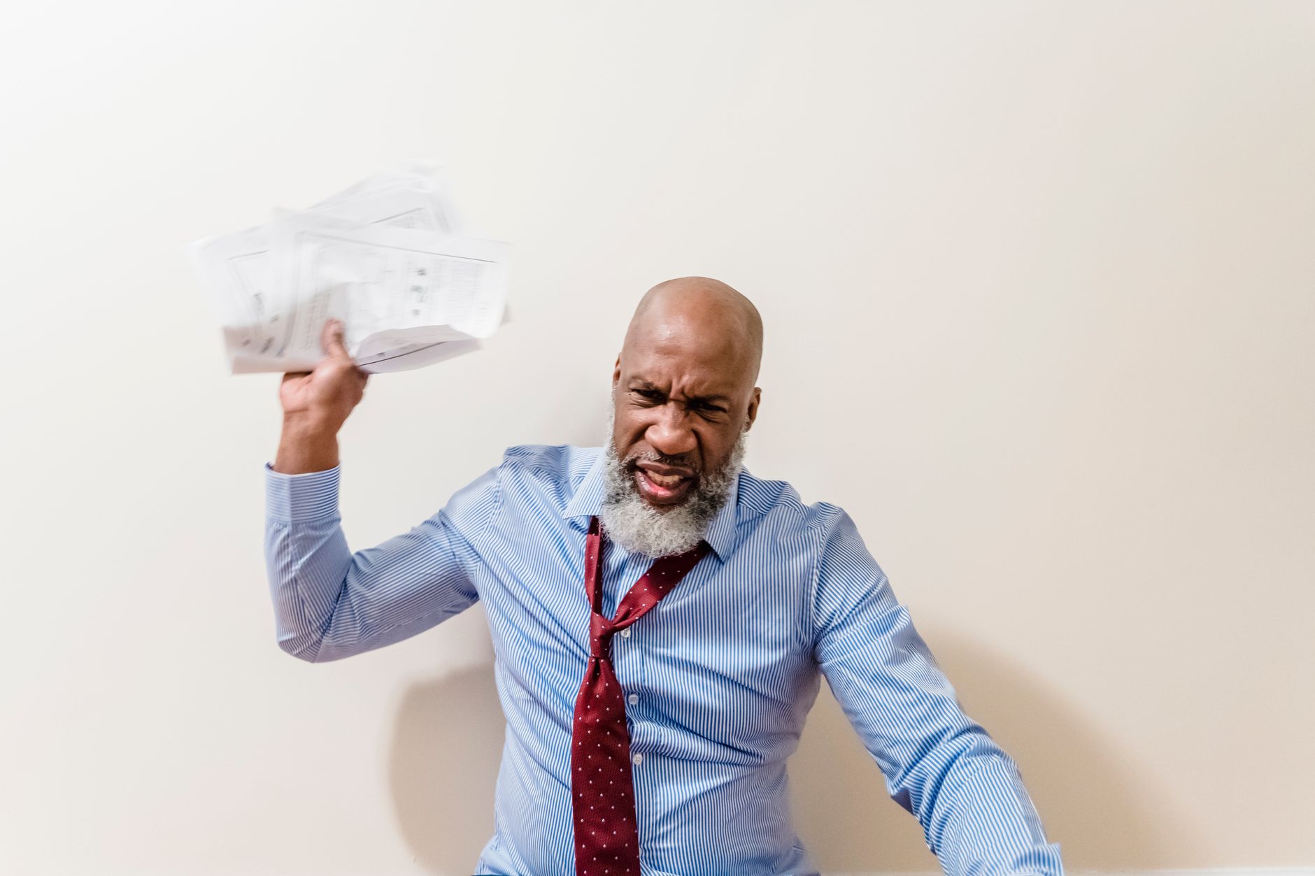 A frustrated bald man with a beard throws papers in anger, expressing intense emotion.