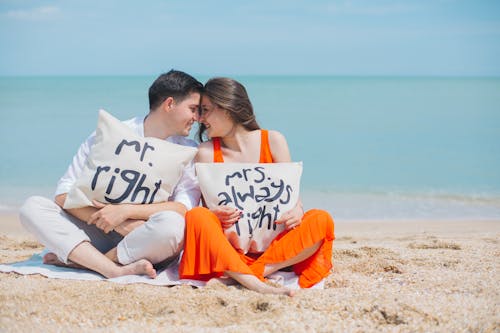無料 海岸近くの茶色の砂の上に座っている服を着ている男性と女性 写真素材