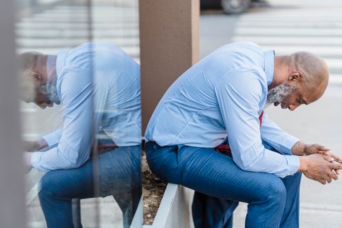 Free A thoughtful man in a suit sits in reflection on an urban street, embodying contemplation. Stock Photo